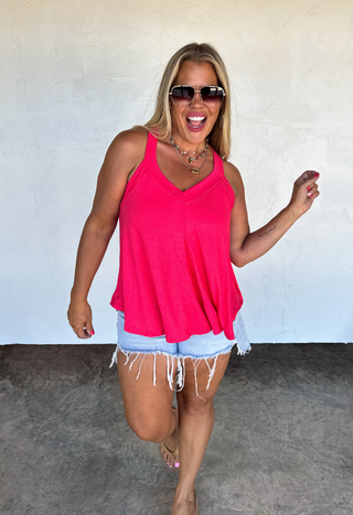 Woman wearing a pink tank top and denim shorts against a plain background